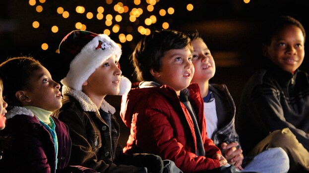 A little boy in a Mickey Mouse Santa hat sitting with 4 other children