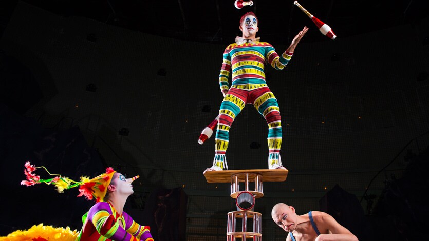 A juggler balancing on a platform above a strongman and a clown