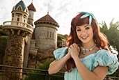 Ariel stands with her hands clasped in front of Prince Eric's castle
