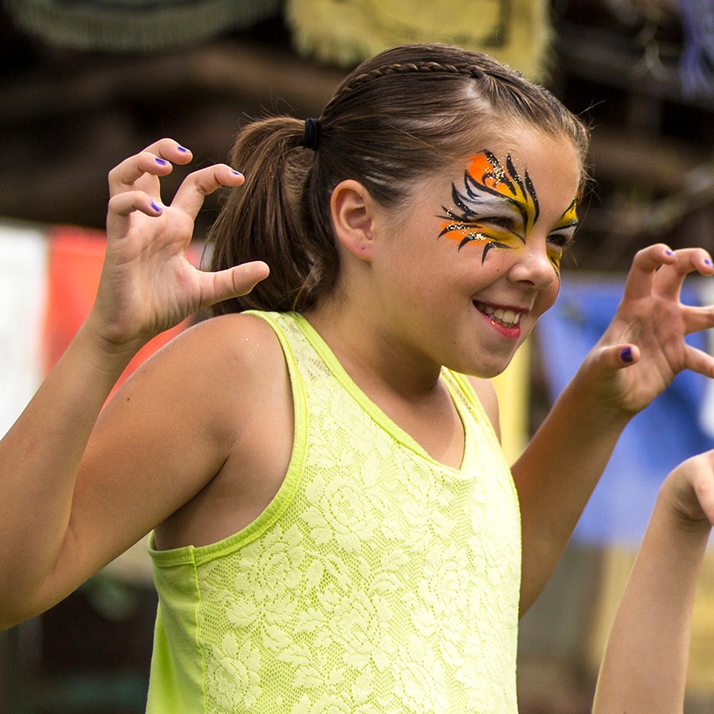 A young female Guest in ferociously themed face paint smiles while posing for a picture