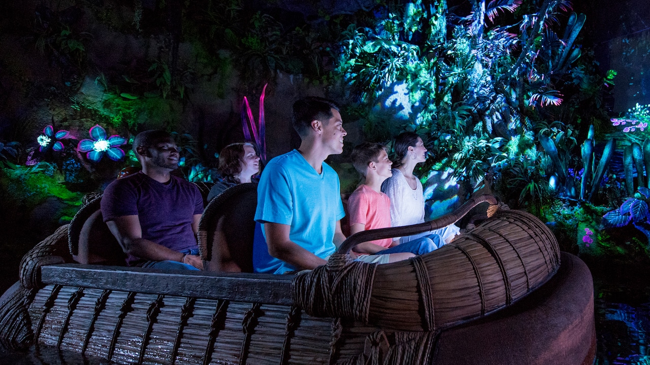 A family looks on in wonder while riding a reed raft through the bioluminescent Na'vi River Journey