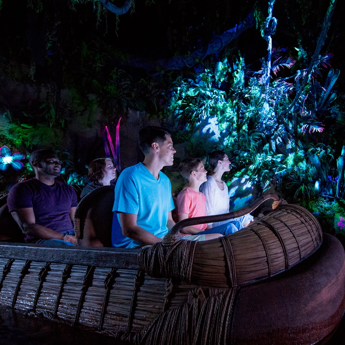 A family looks on in wonder while riding a reed raft through the bioluminescent Na'vi River Journey